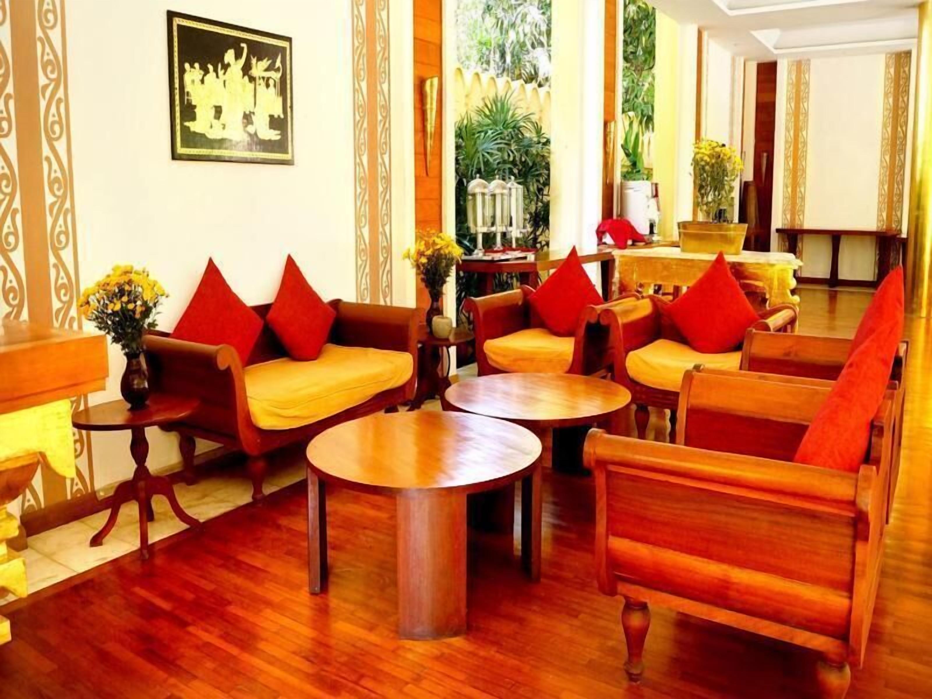 Un salón de estilo tradicional con muebles de madera, cojines rojos y una obra enmarcada en la pared.