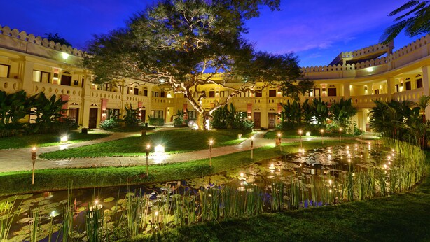 A courtyard with a large tree, a pond, and a building with multiple balconies and lights. - Areindmar Hotel (Nyaung-U)