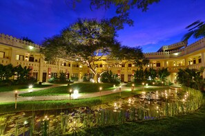 A courtyard with a large tree, a pond, and a building with multiple balconies and lights. - Areindmar Hotel (Nyaung-U)