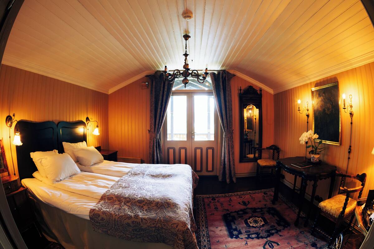 A bedroom with a large bed, a chandelier, a desk, and a chair.