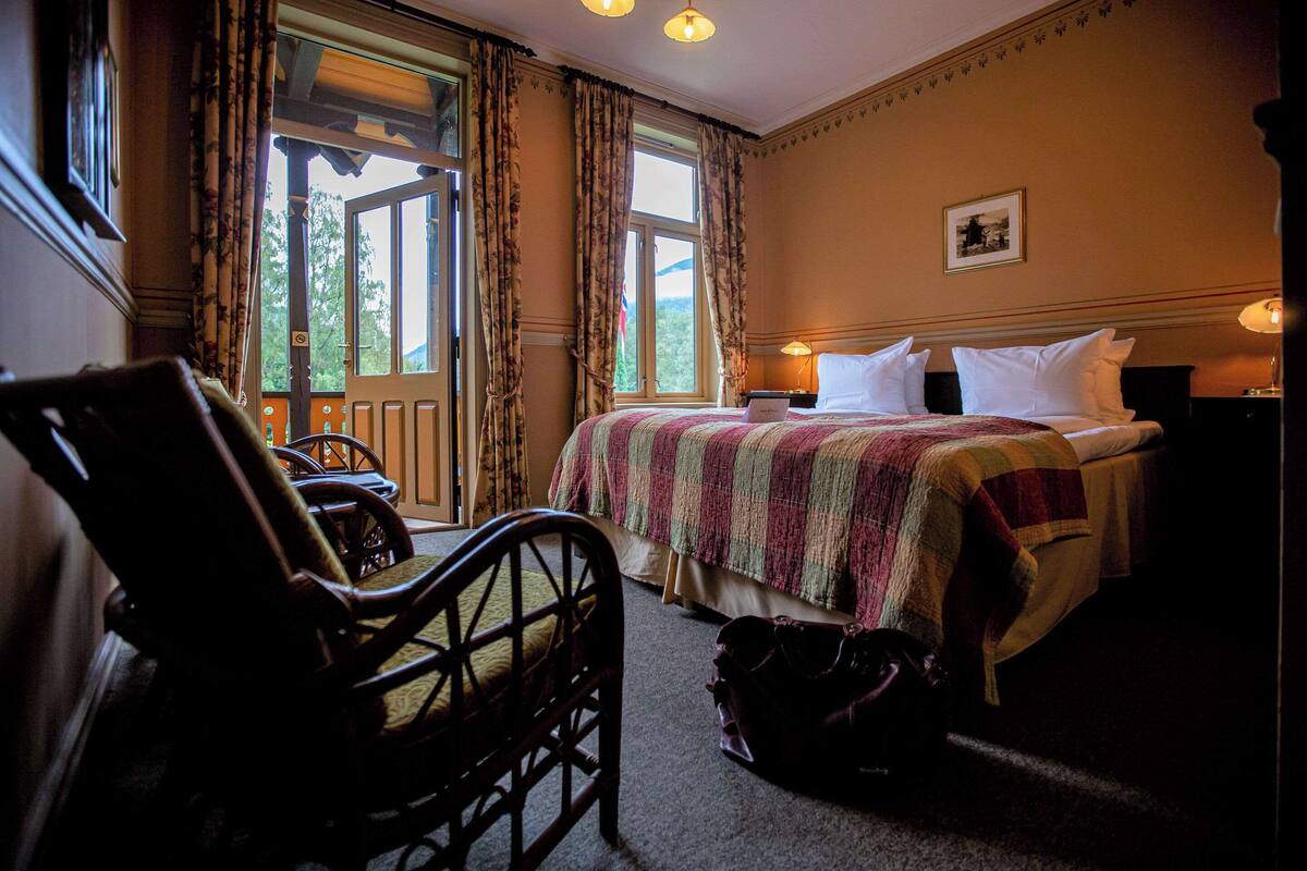 A hotel room with a bed, a chair, a desk, and a window with curtains.
