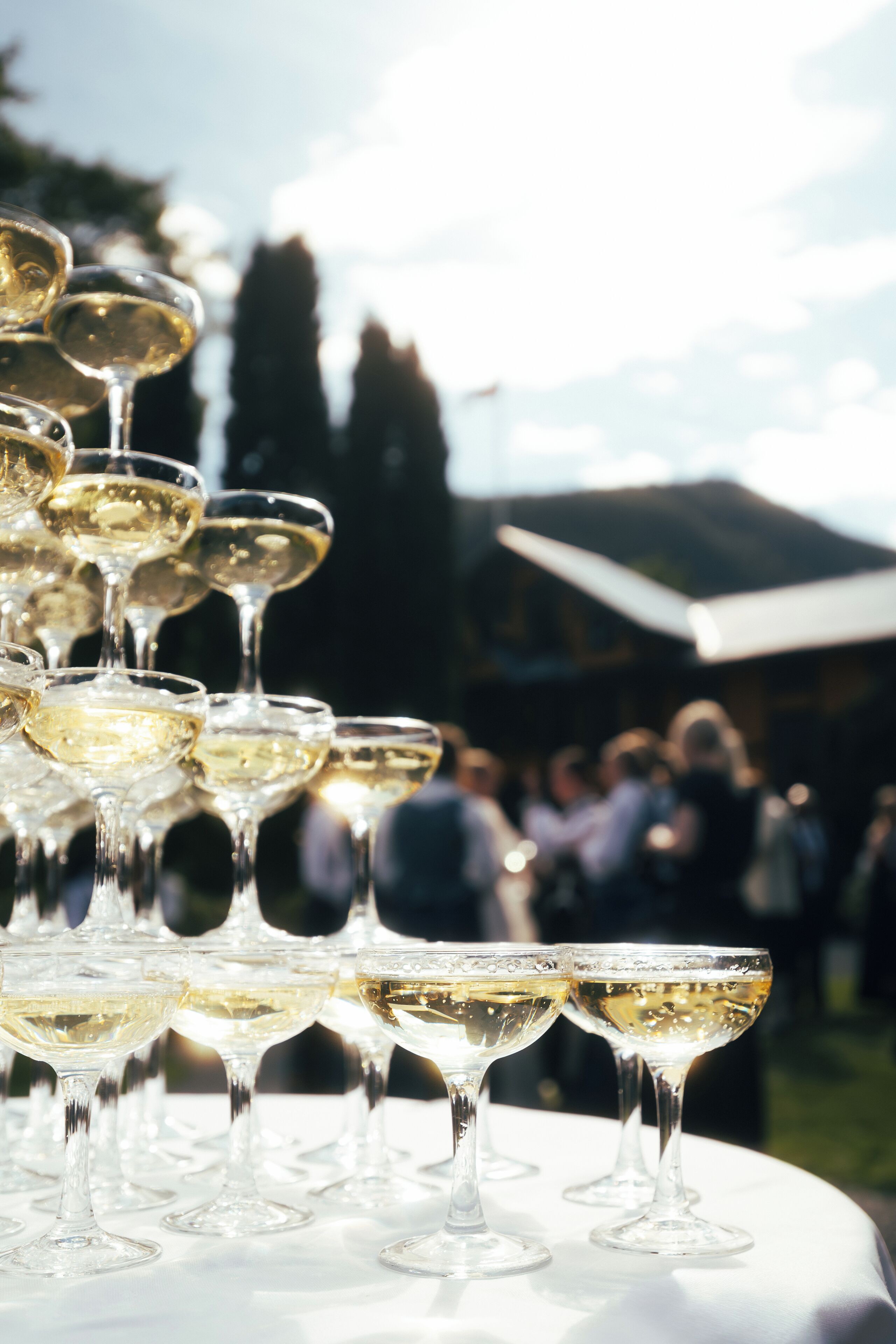 A table with multiple wine glasses filled with white wine, set outdoors with a crowd in the background.