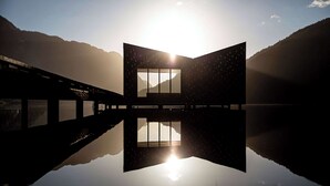A modern building with a large window reflecting on a calm body of water, surrounded by mountains. - Dalen Hotel (Tokke)
