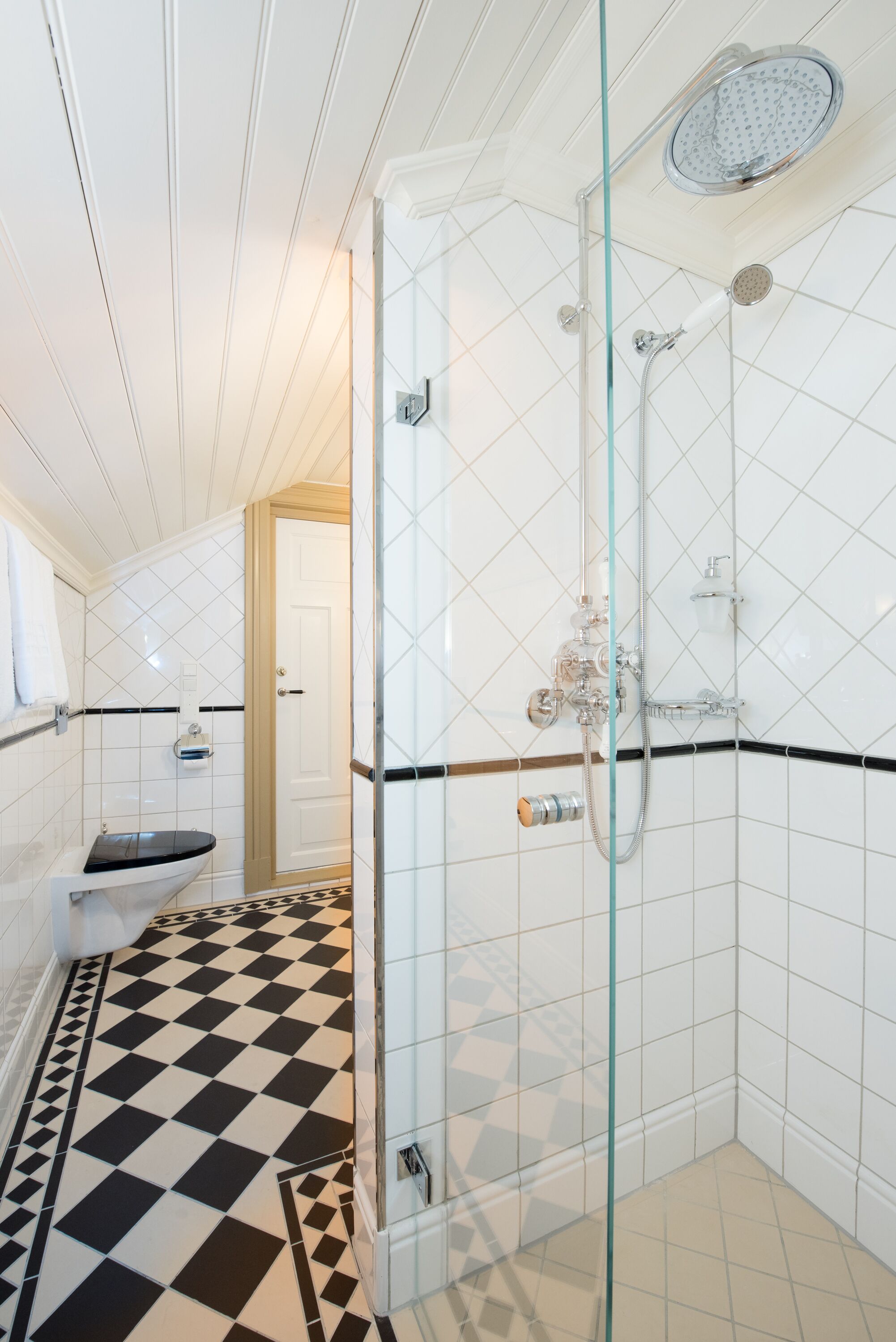 A bathroom with a glass shower enclosure, a toilet, and a checkered floor.