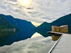 Un lago tranquillo con un molo in legno e un piccolo edificio in mattoni, circondato da rigogliose montagne verdi.