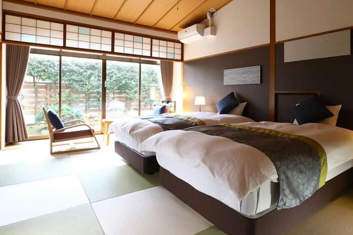 A hotel room with a large bed, a chair, a desk, and a view of greenery outside.