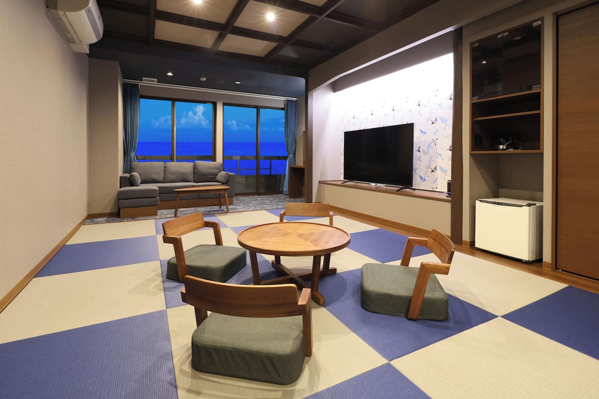 A room with tatami mats, a sofa, a TV, and a view of the sea.