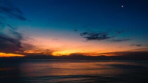 A sunset over a calm sea with a distant mountain range.