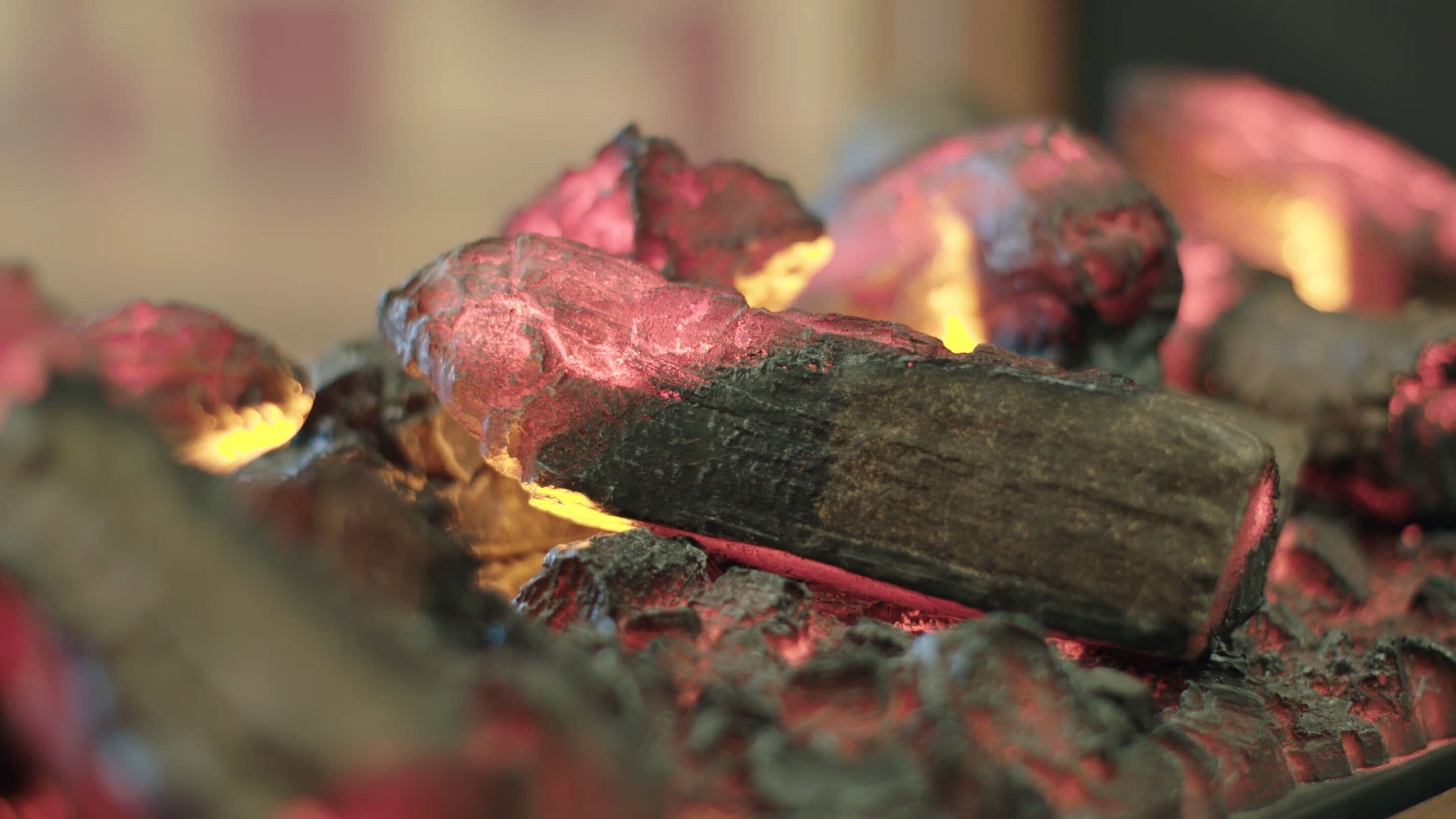 A close-up of glowing charcoal with a wooden stick partially burning.