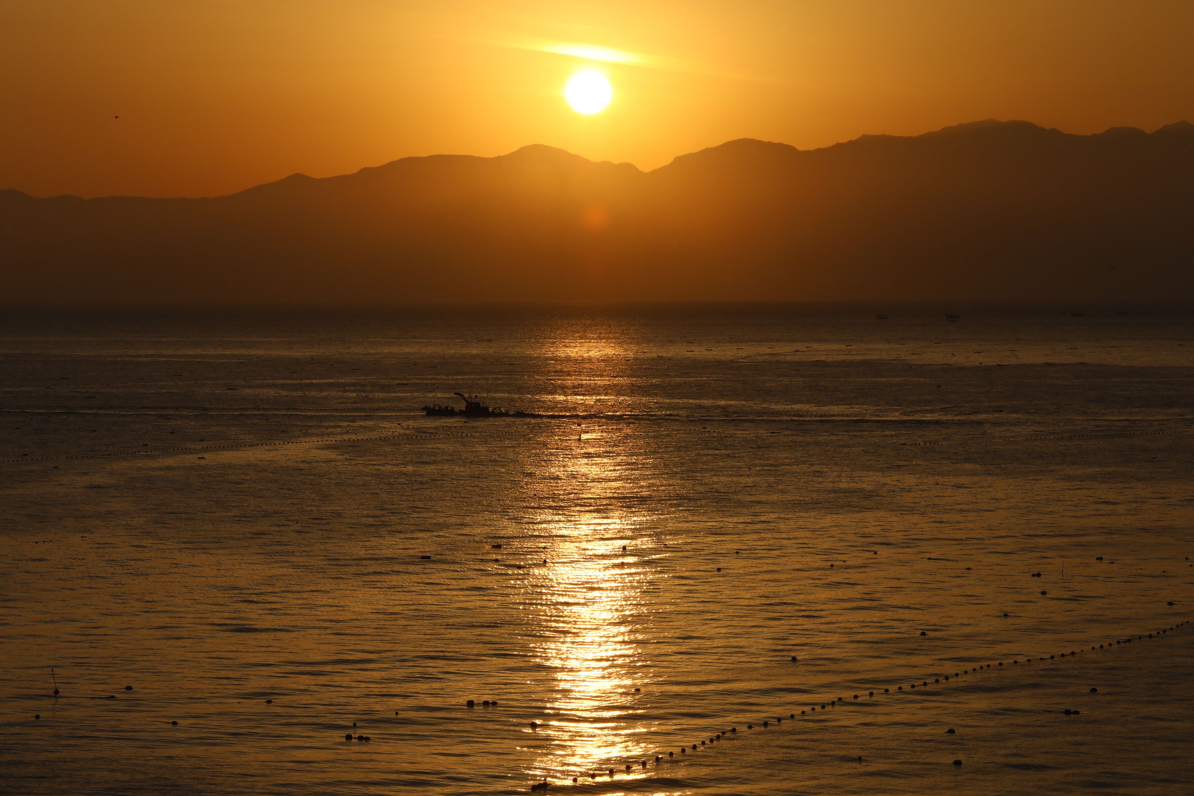 A sunset over a calm sea with distant mountains.