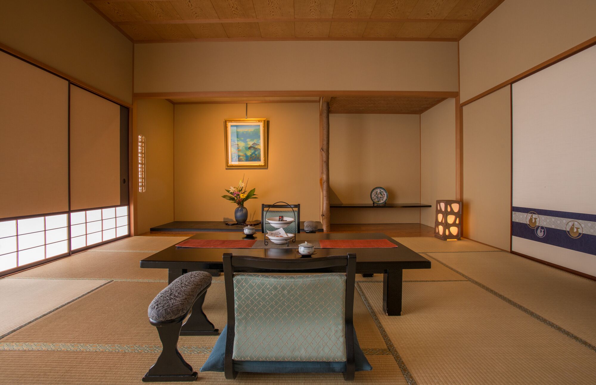 A traditional Japanese room with tatami flooring, a low table with a tea set, a chair, and a painting on the wall.