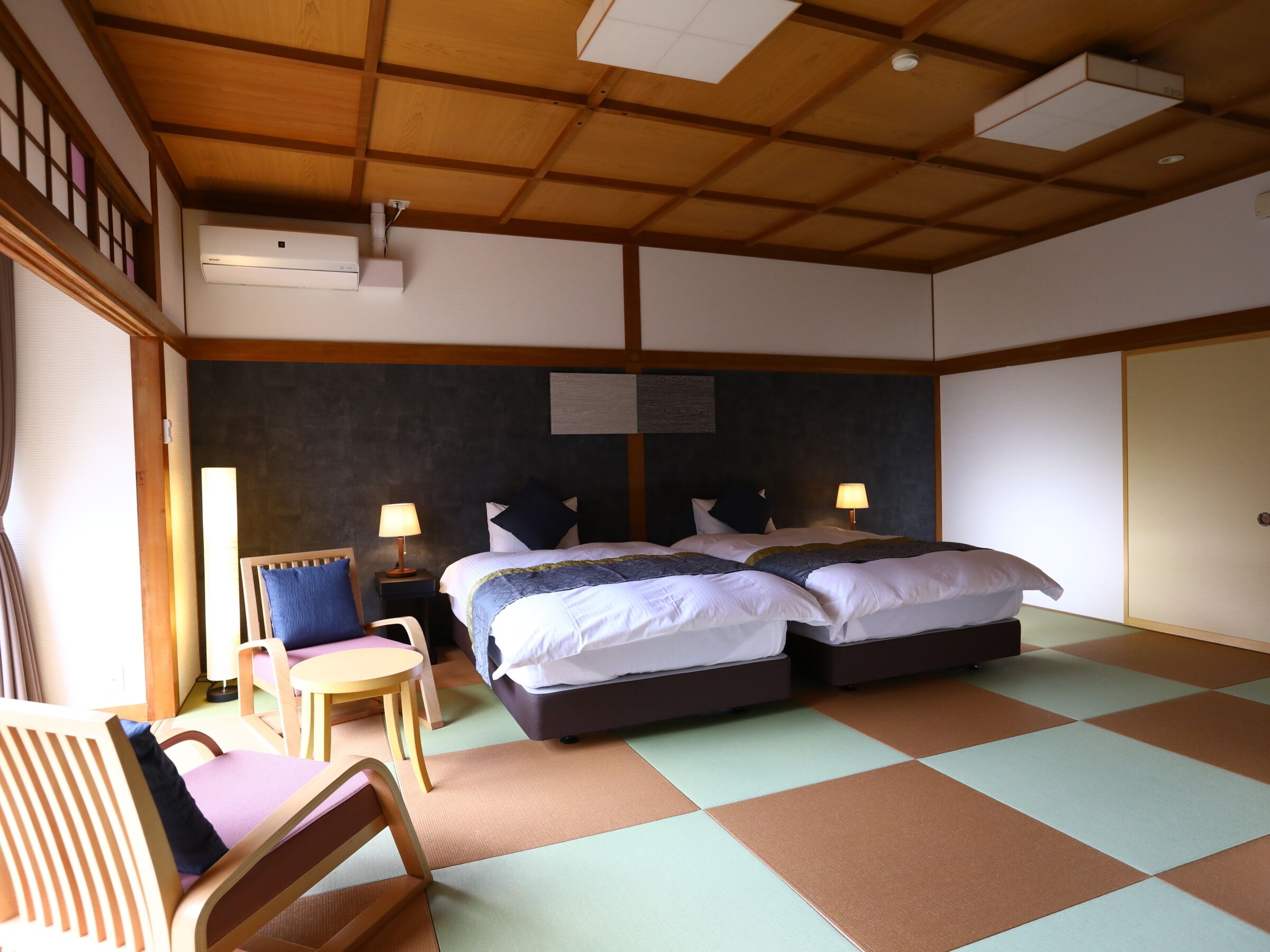 A hotel room with two beds, a chair, a table, and a ceiling fan.