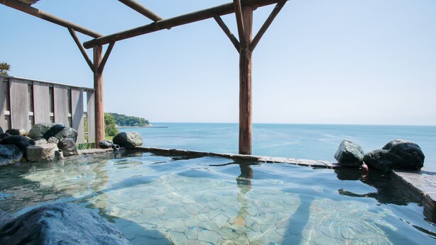 Una piscina cristalina con rocas y una pérgola de madera con vistas al mar.