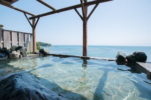 Una piscina cristalina con rocas y una pérgola de madera con vistas al mar.