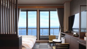 Habitación de hotel con cama, escritorio, silla, televisión y un amplio ventanal con vista al mar.