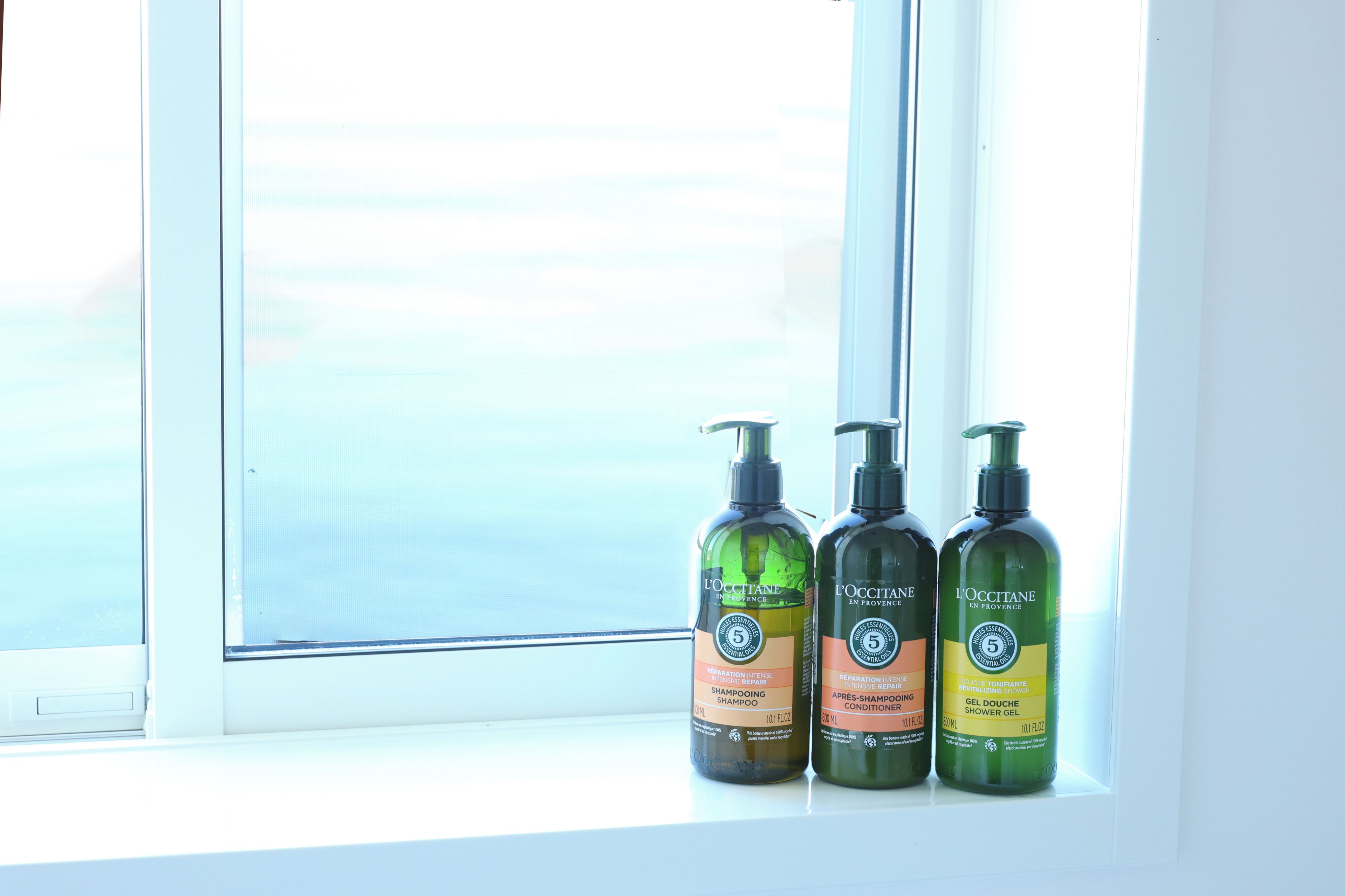 Three bottles of L'OCCITANE products on a windowsill.