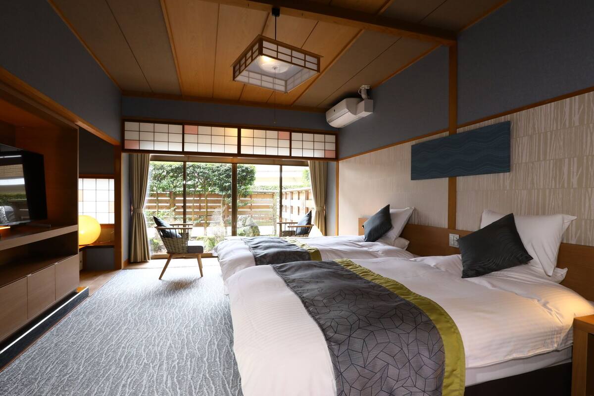 A hotel room with two beds, a TV, a desk, and a view of the outdoors.