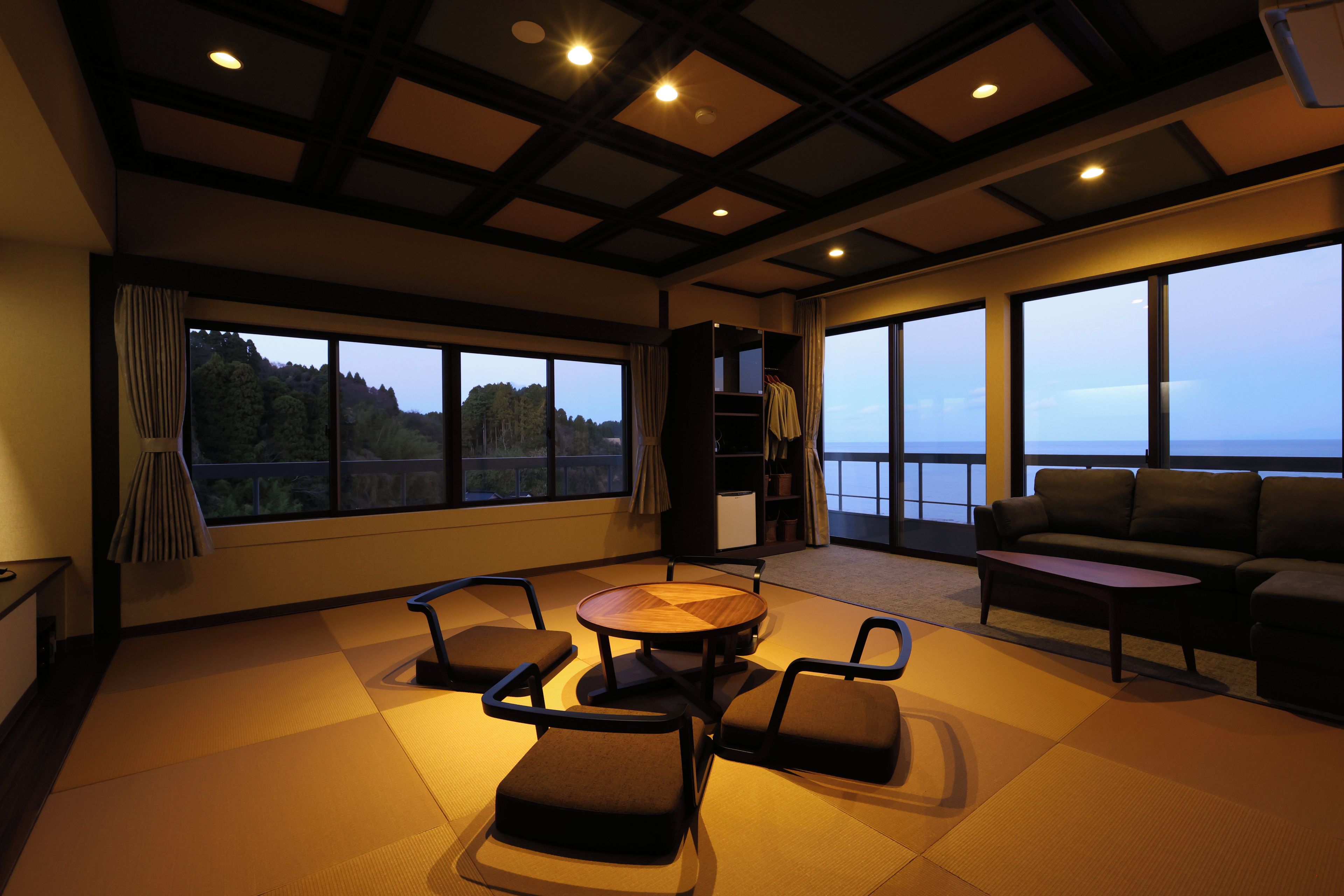 A modern living room with a large window, a sofa, a coffee table, and a bookshelf.