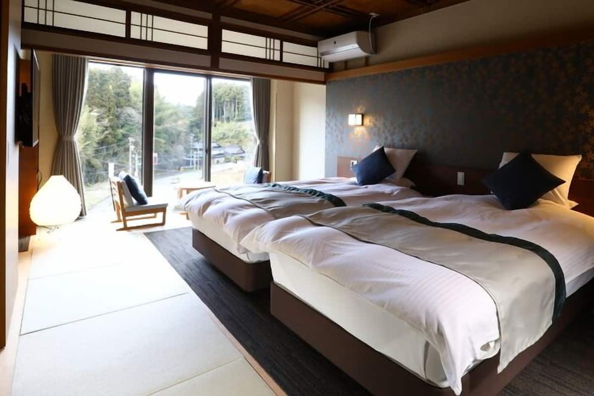 A hotel room with a large bed, two bedside tables, a window with curtains, and a view of the outdoors.