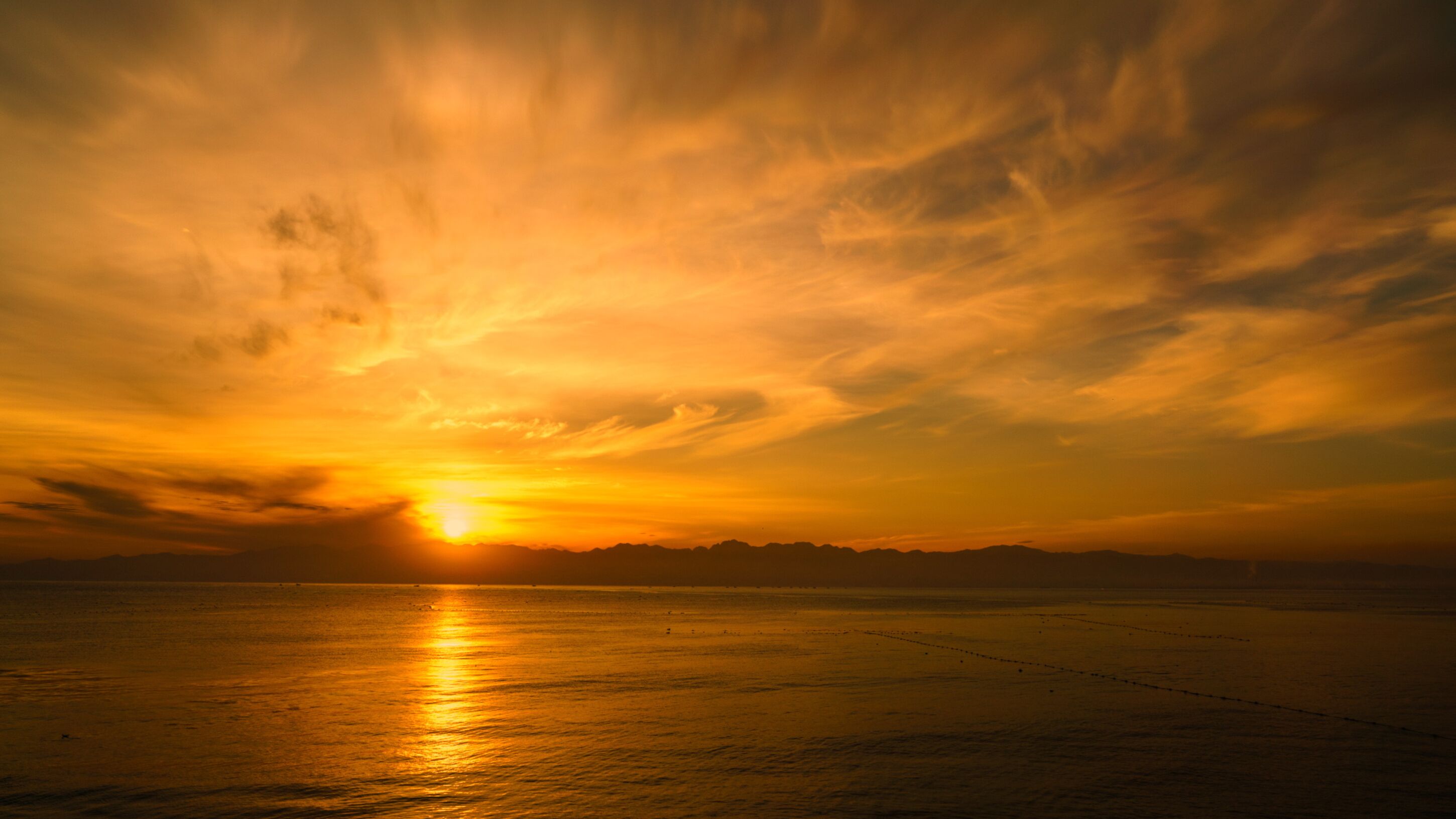 Un atardecer sobre un mar tranquilo con una cadena montañosa distante.