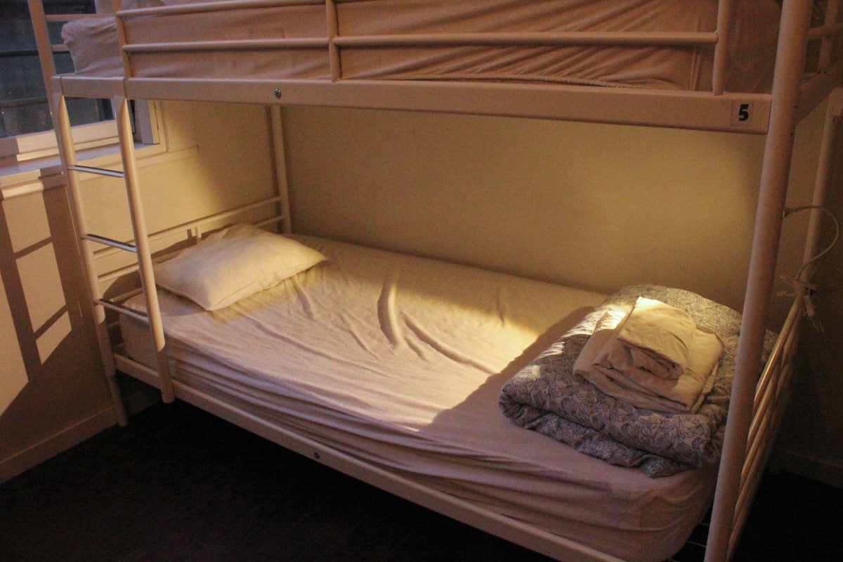 A bunk bed with a single bed on the lower bunk and a mattress on the upper bunk.