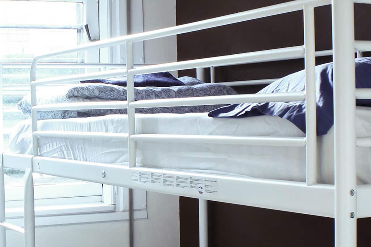 A bunk bed with white metal railings and a window to the left.