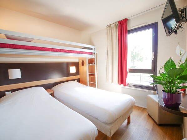 A hotel room with a bunk bed, a desk with a computer, a window with curtains, and a potted plant.