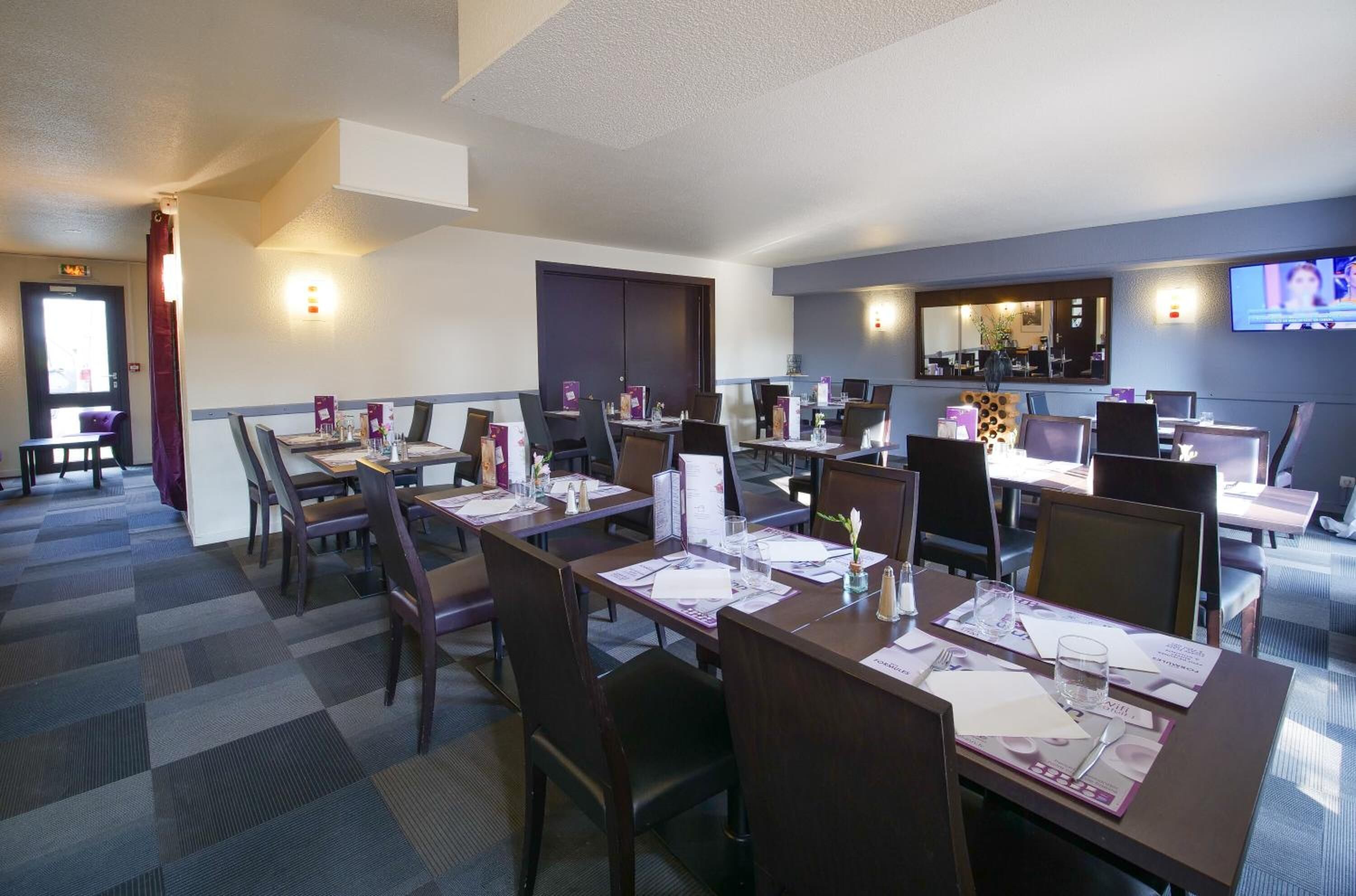 Un comedor de hotel con varias mesas y sillas, una pantalla de televisión y una zona de bar.