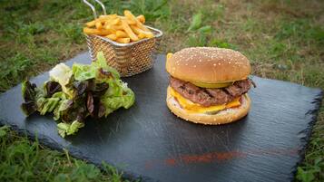 Hamburguesa con lechuga, queso y pan, acompañada de papas fritas y una ensalada en una tabla de pizarra.