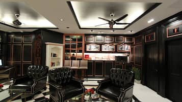 A hotel lobby with black leather sofas, a checkered floor, a glass coffee table with a vase, and a reception desk.