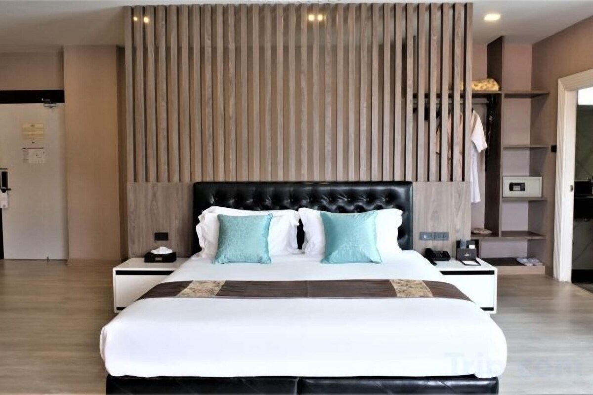 Une chambre d’hôtel moderne avec un grand lit, une tête de lit en lattes de bois, une table de chevet et une petite table de nuit.