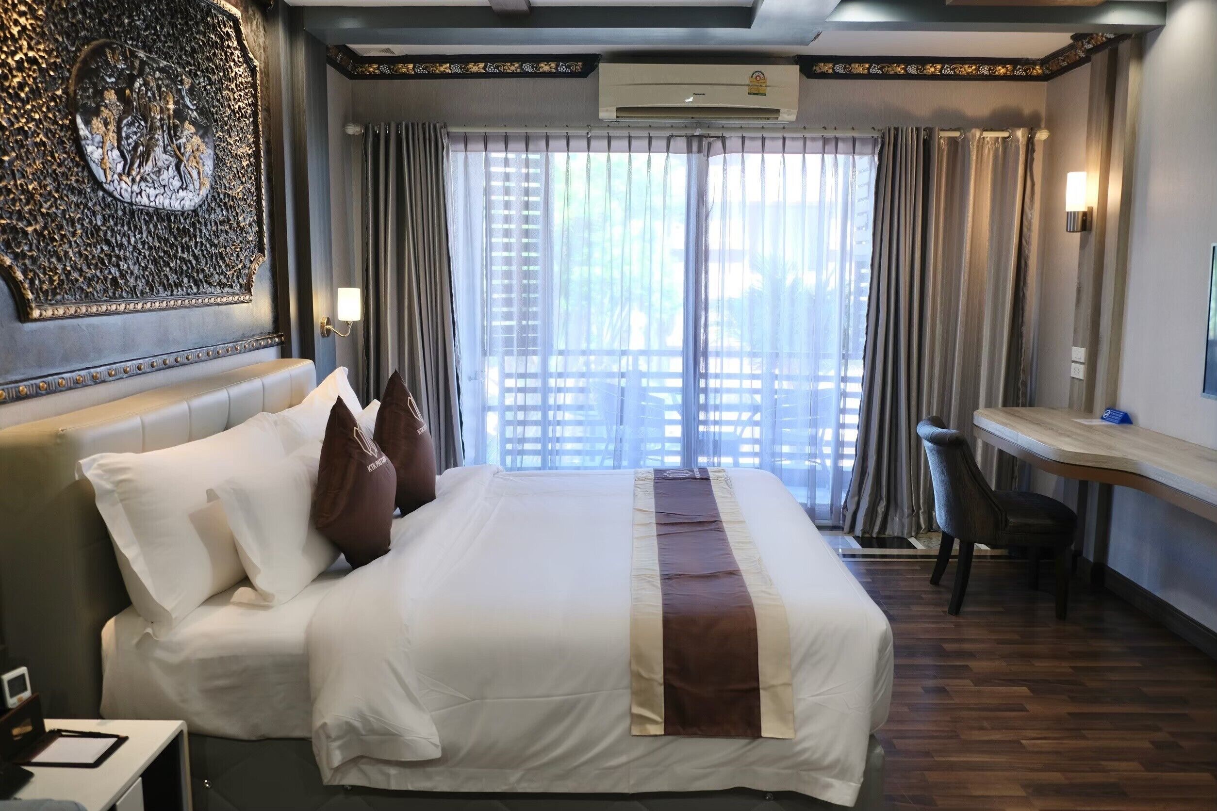 A hotel room with a large bed, a desk, and a view through the window.