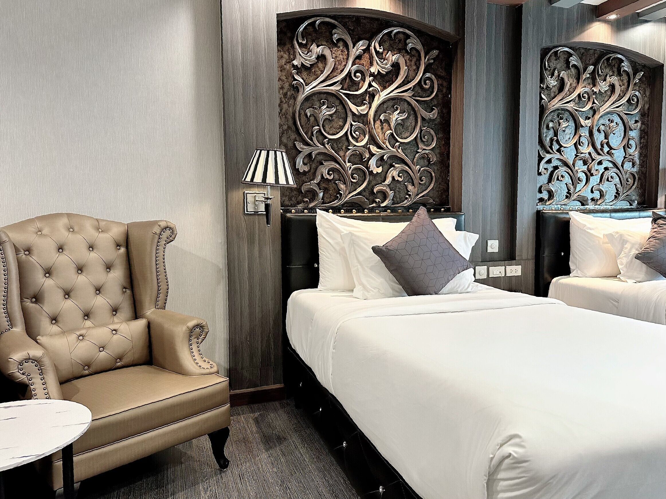 A hotel room with a tufted armchair, a bed with white linens, and decorative wall panels.