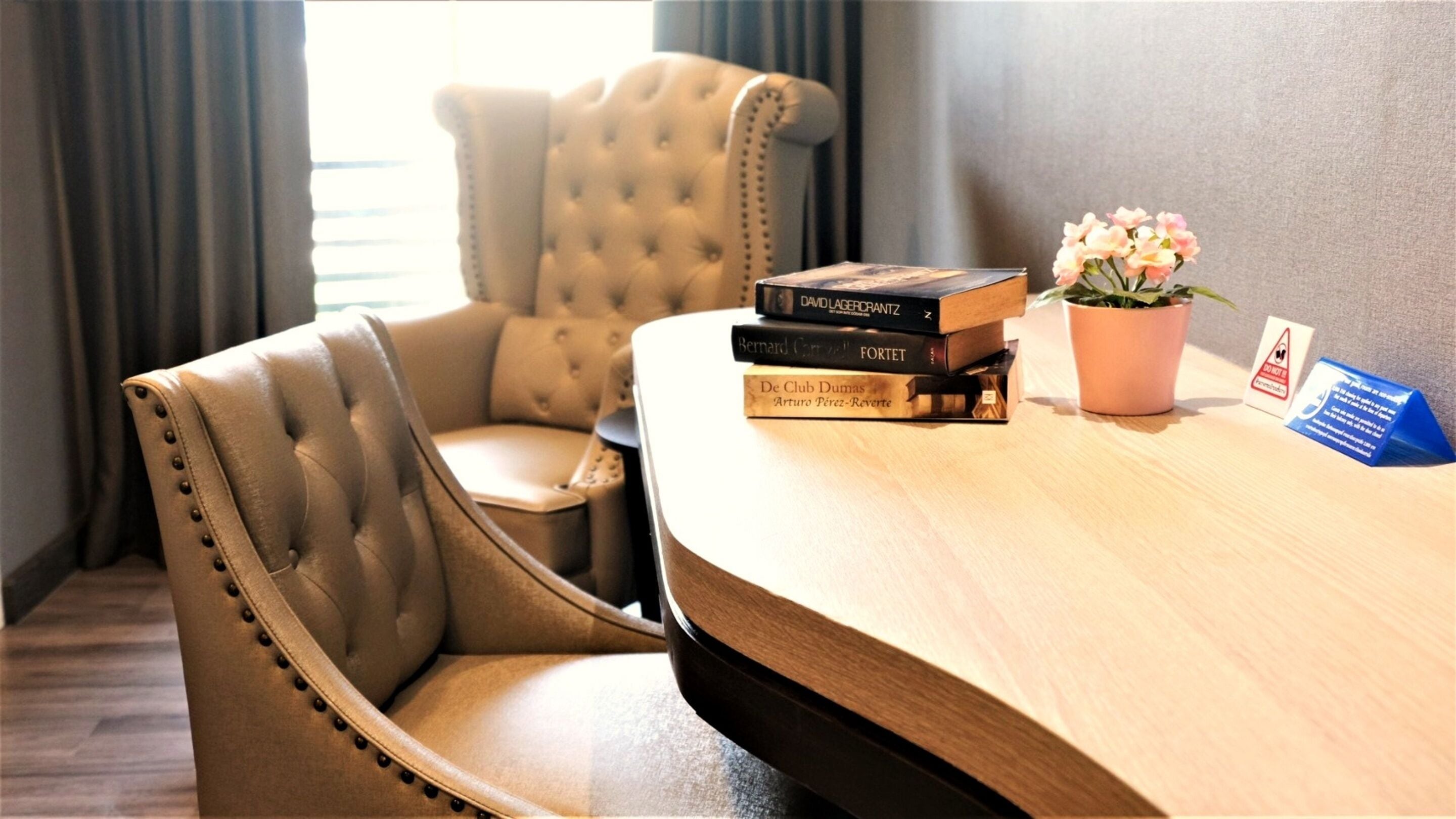 A hotel room with a tufted leather armchair, a wooden desk with books and a potted plant, and a 'Do Not Disturb' sign.