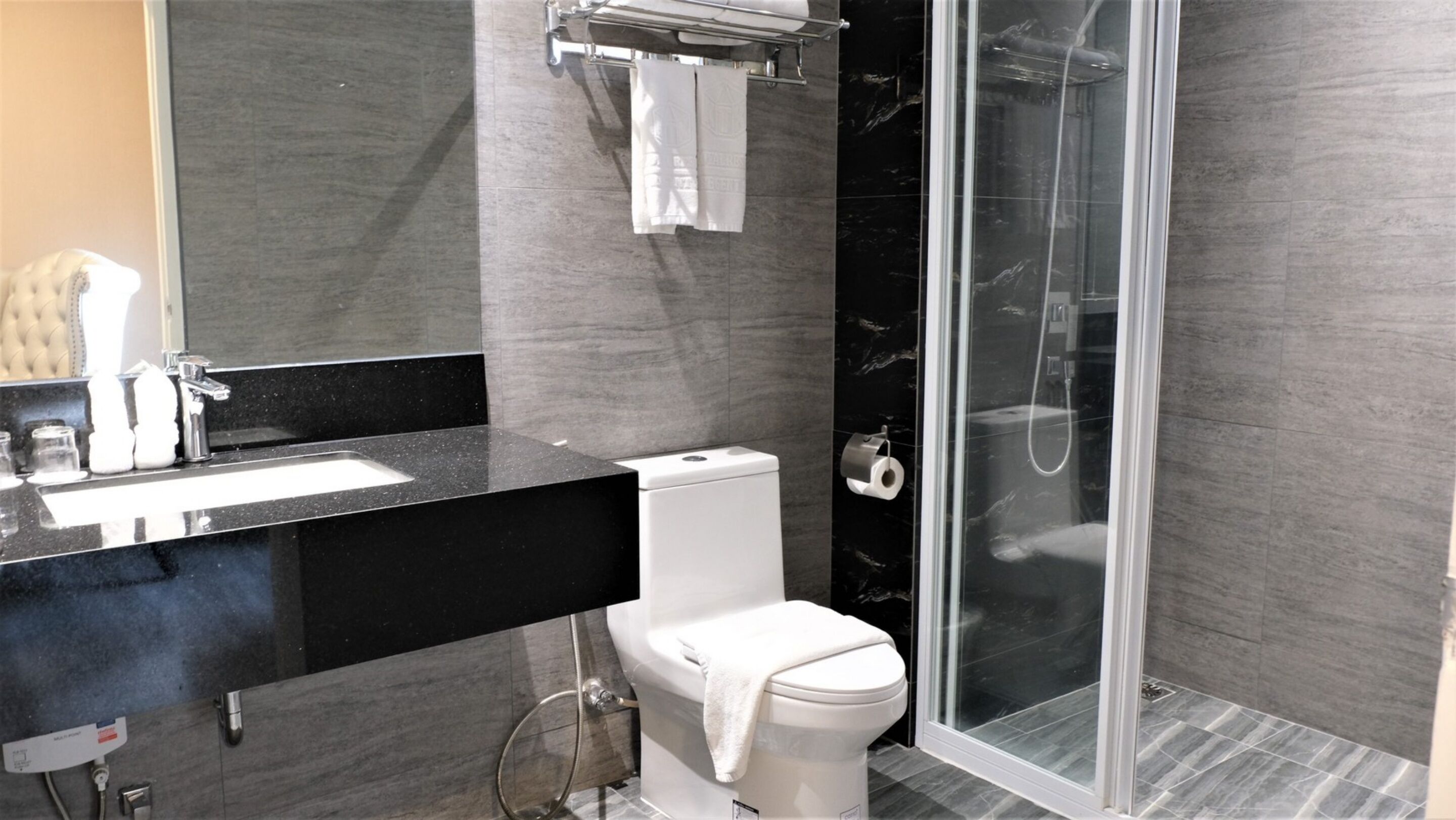 Une salle de bain moderne avec un lavabo sur un plan de toilette noir, des toilettes blanches, une douche à parois de verre et un pare-baignoire en marbre.