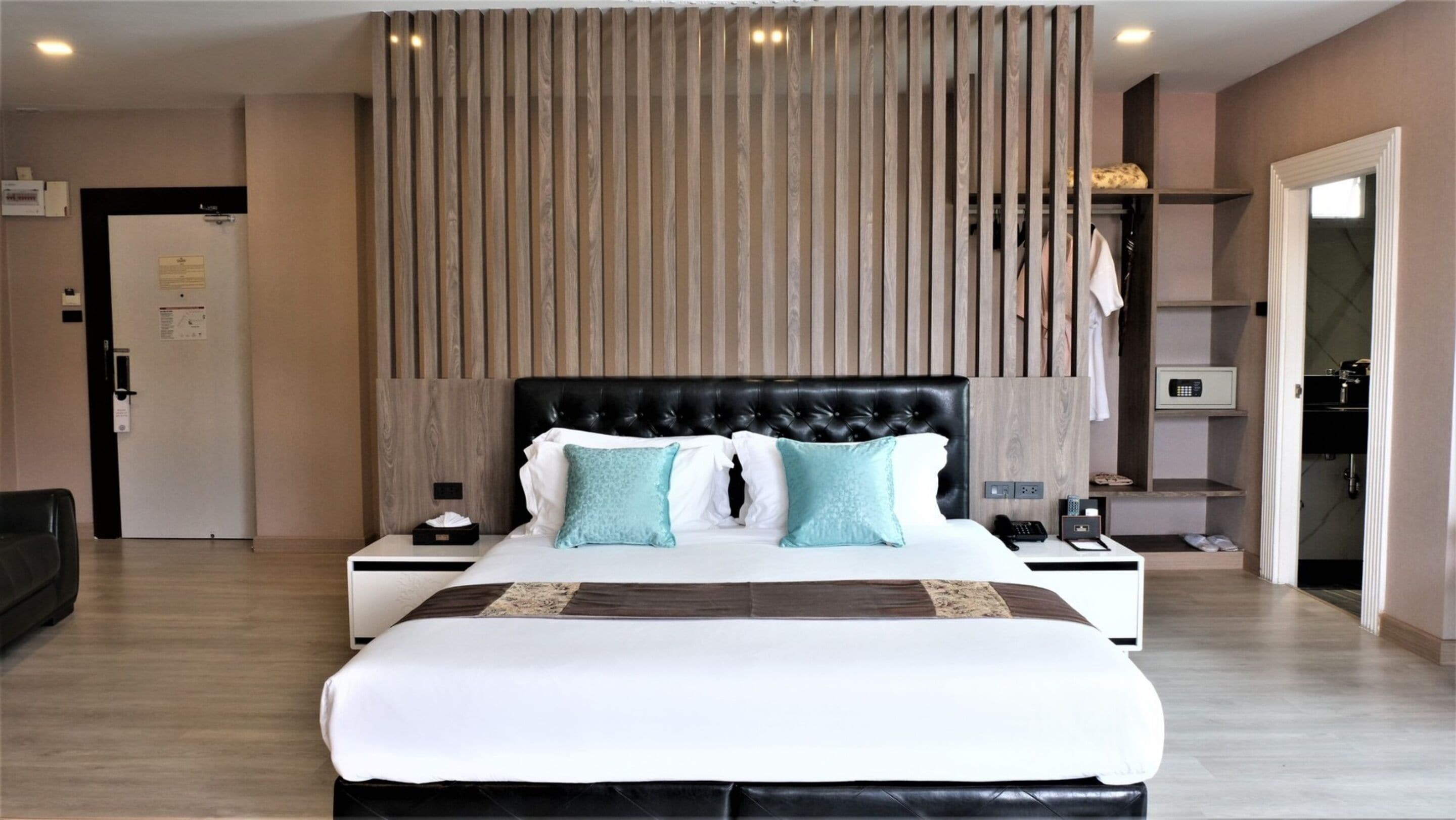 Een moderne hotelkamer met een groot bed, een houten lattenkap, een nachtkastje met lamp en een kledingkast.