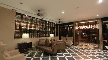 A lobby with a checkered floor, a sofa, armchairs, a glass coffee table, a lamp, and a wall with framed pictures.