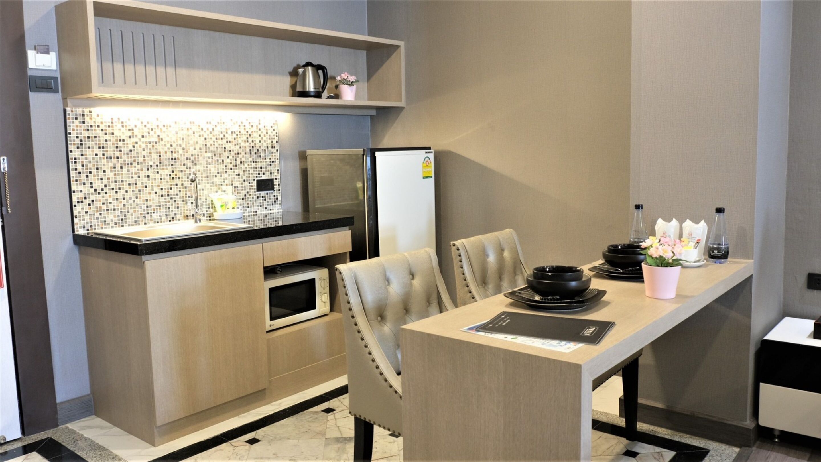 A compact kitchen with a microwave, oven, and a refrigerator. There is a dining table with chairs and a small potted plant.
