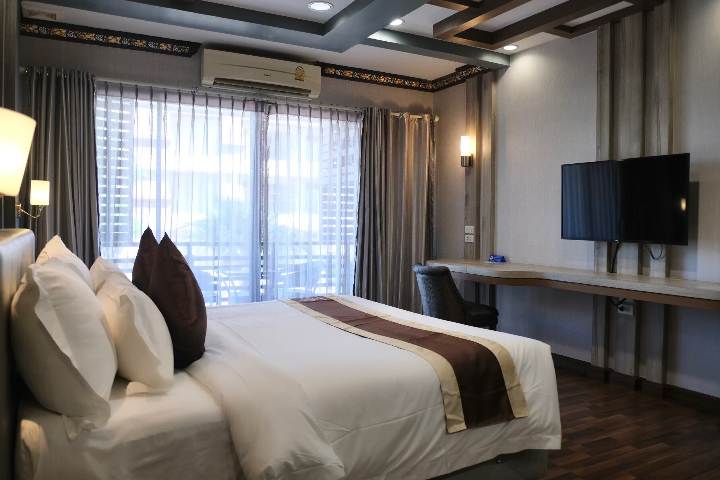 Ein Hotelzimmer mit einem großen Bett, einem Schreibtisch, einem Flachbildfernseher und Blick auf die Stadt durch große Fenster.
