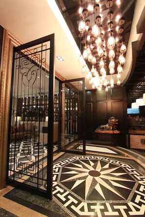 A lobby with a geometric patterned floor, a decorative metal gate, and a modern chandelier.