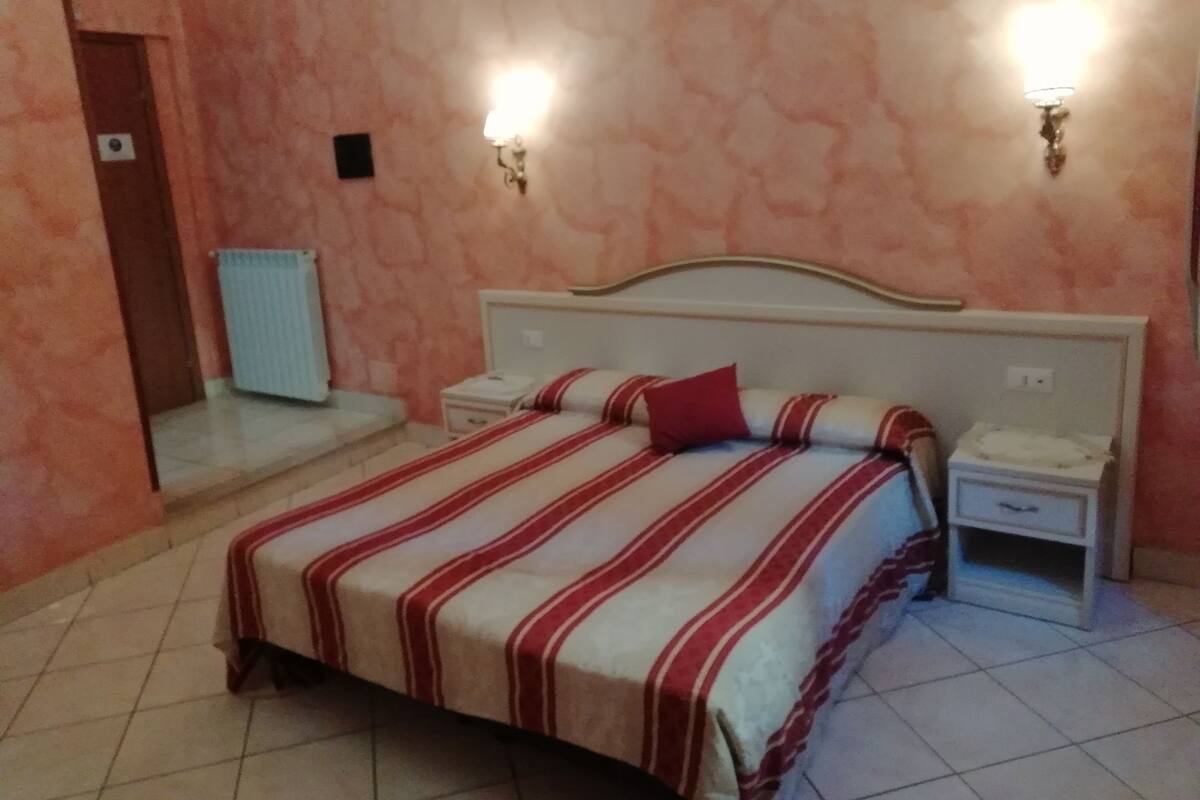 A bedroom with a bed, two bedside tables, a nightstand, a radiator, and wall-mounted lights.