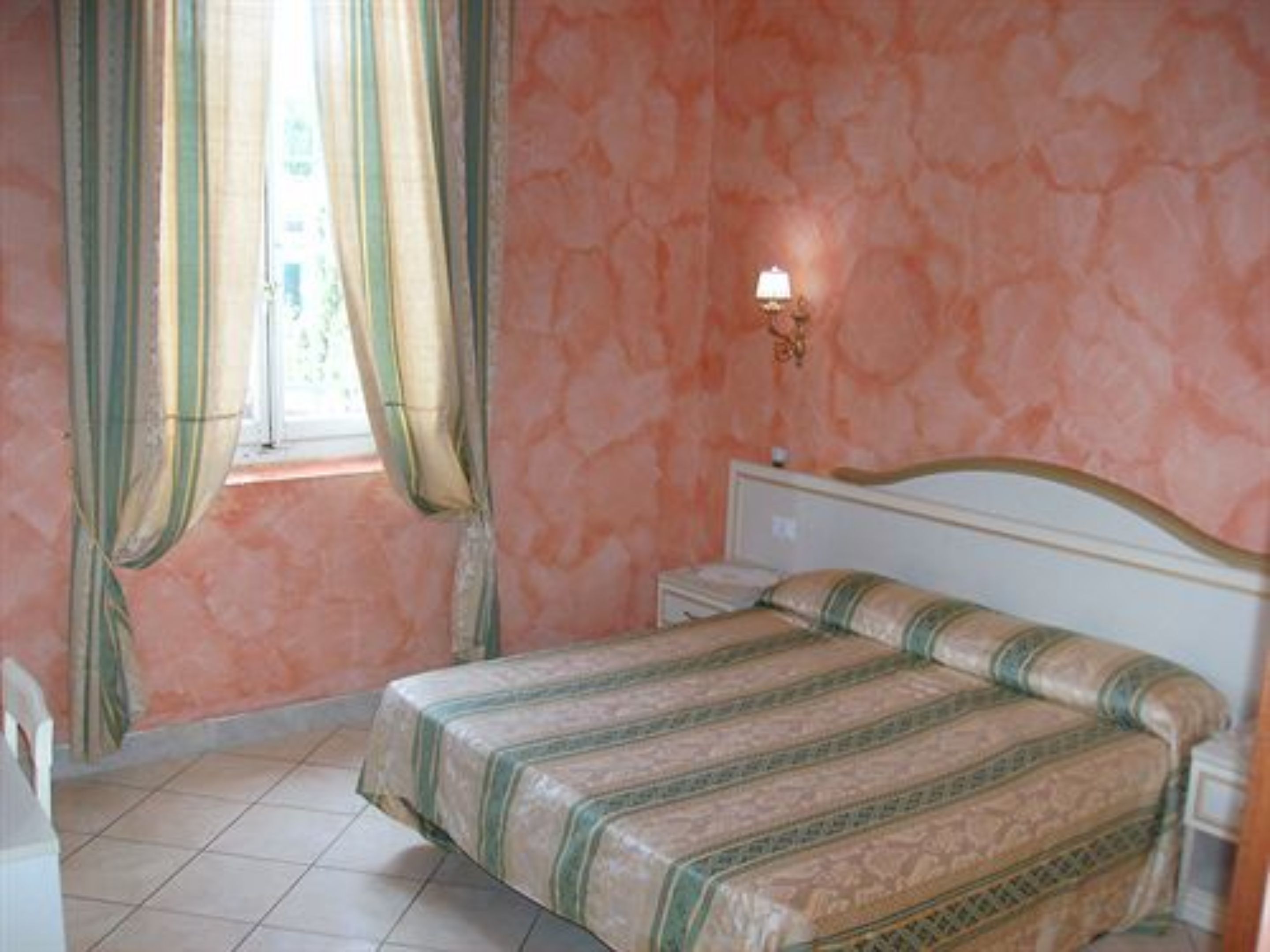 Une chambre à coucher avec un lit, une table de chevet, une lampe, des rideaux et une fenêtre.