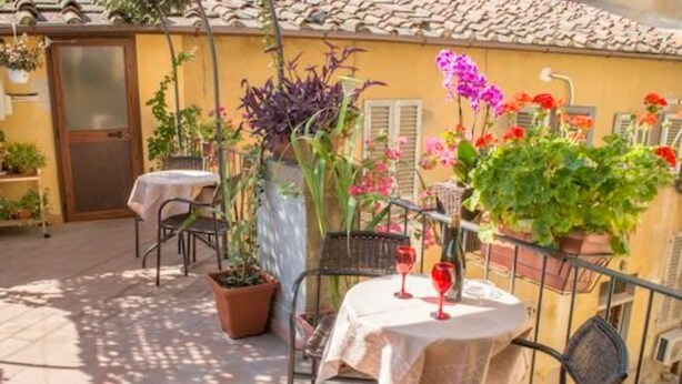 An outdoor patio with a table and chairs, surrounded by potted plants and flowers.