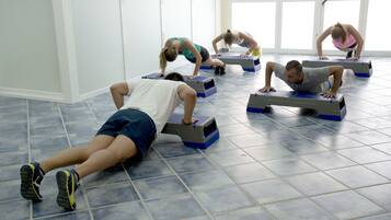 Un grupo de personas haciendo flexiones sobre plataformas de ejercicio azul y gris en una habitación con suelo de baldosas y ventanas amplias.