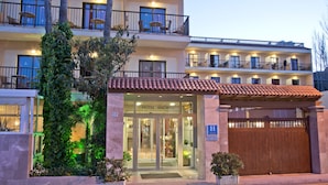 Un hotel con entrada de vidrio, un balcón con sillas y un techo de tejas.