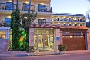 Un hotel con entrada de vidrio, un balcón con sillas y un techo de tejas.