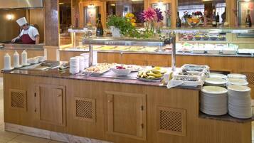A buffet area with various food items, a chef in the background, and a floral arrangement.