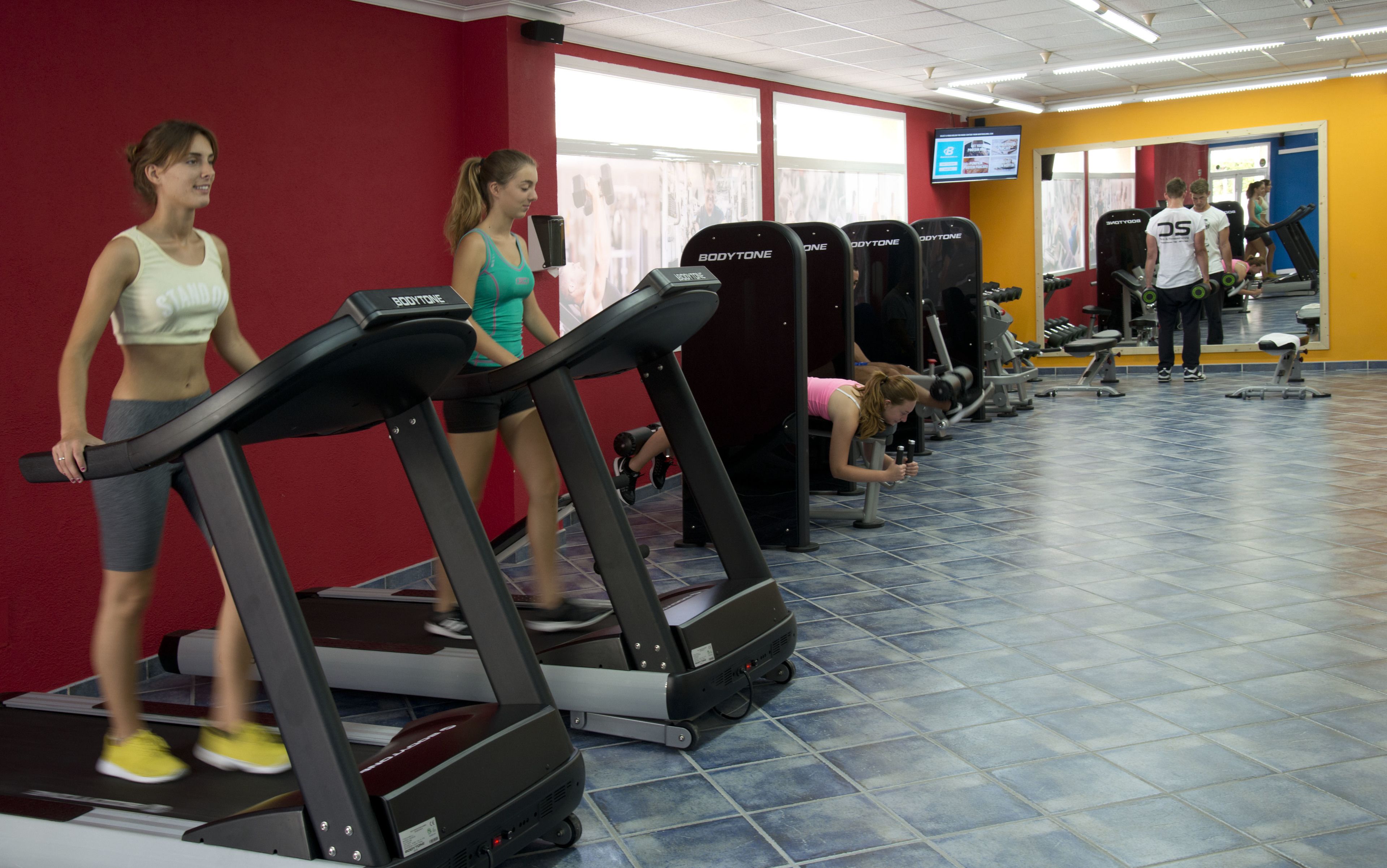 Un gimnasio con cintas de correr, pesas y una pantalla de televisión.