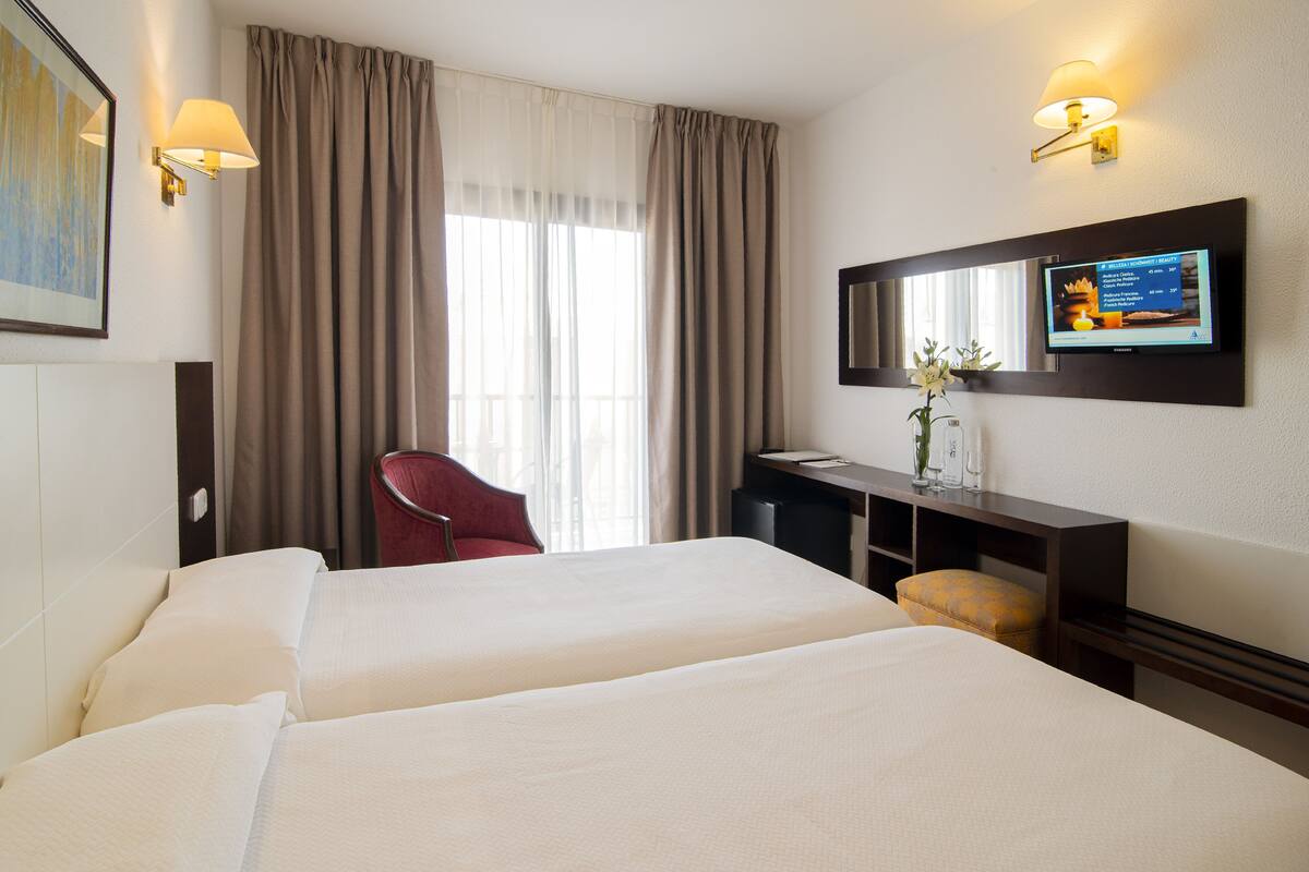 A hotel room with two beds, a desk with a computer, a chair, and a TV mounted on the wall.