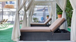 Una tumbona con asiento y respaldo acolchados, ubicada bajo un toldo con cortinas blancas.